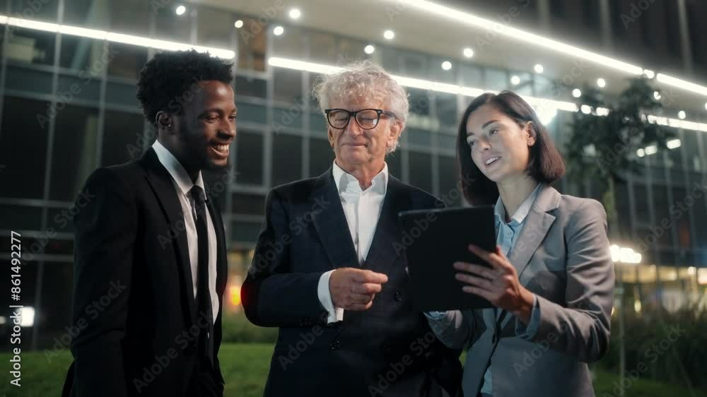 Senior boss talking to workers outside at night. Men and woman communicating near modern business center. Male and female in official clothes creating business strategy outdoor. Ethnic diversity. Senior boss talking to workers outside at night. Men and woman communicating near modern business center. Male and female in official clothes creating business strategy outdoor. Ethnic diversity.