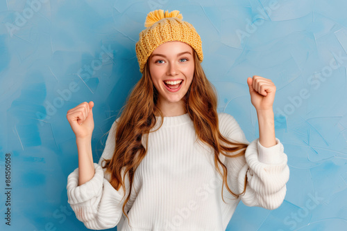 excited girl  in sweater smile cheerfuly rise her fists on isolated blue  background  photo