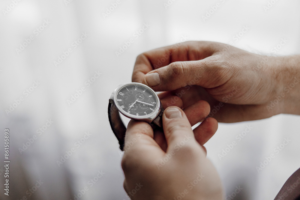 A man is holding a watch in his hand. The watch is black and silver. The man is looking at the watch, possibly checking the time A man is holding a watch in his hand. The watch is black and silver. The man is looking at the watch, possibly checking the time