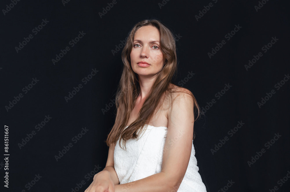 Portrait of an attractive middle-aged woman with long hair wrapped in white towel on black background Portrait of an attractive middle-aged woman with long hair wrapped in white towel on black background