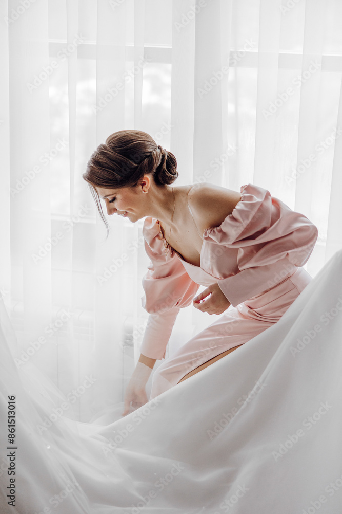 A woman in a pink dress is standing in front of a white curtain. She is smiling and she is getting ready for a special occasion A woman in a pink dress is standing in front of a white curtain. She is smiling and she is getting ready for a special occasion