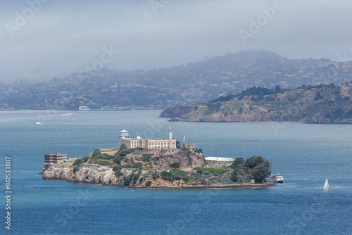 Alcatraz Island in the San Francisco Bay with a misty mountain backdrop. Iconic historic prison landmark viewed from the water on a hazy day in California
