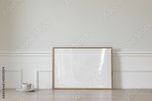 Fototapeta Naklejka Na Ścianę i Meble -  Modern Scandinavian living room interior. Horizontal wooden poster, picture frame mockup on office table. Cup of coffee, tea. White wall background. Elegant stucco dado rail decor. Empty copy space.