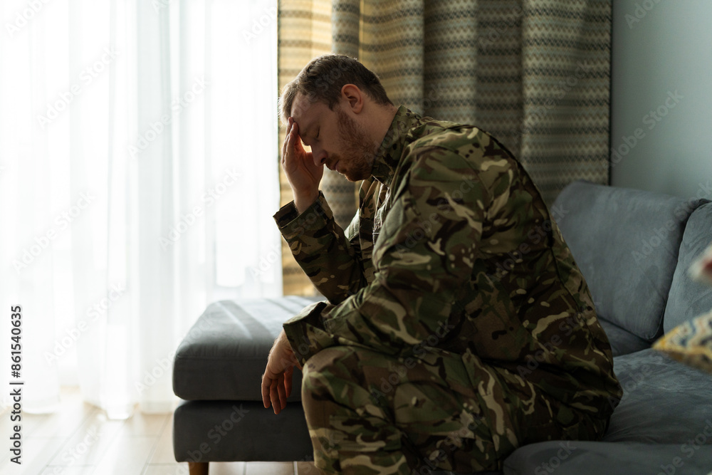 Sad military man sitting at sofa and covering face with hand deep in thoughts Sad military man sitting at sofa and covering face with hand deep in thoughts
