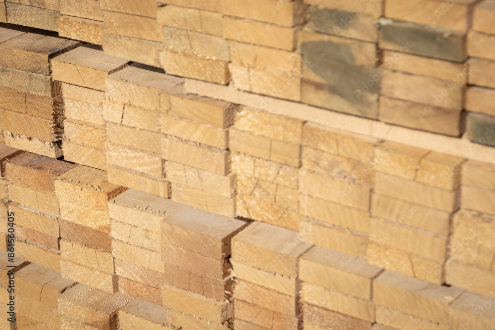Obraz premium Stacked wooden planks in a lumberyard, showing various shades and textures of the wood, arranged in neat rows..
