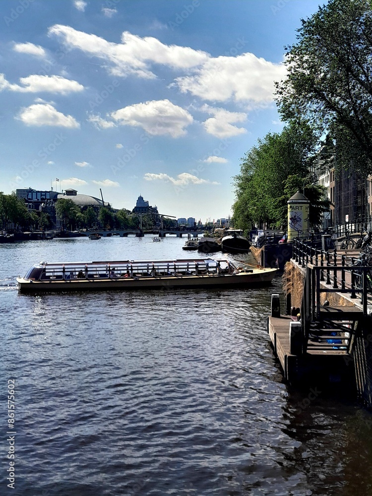 Tour boat turning into canal from the Amstel river in Amsterdam with flower arrangement in the foreground, on a clear sunny day in Amsterdam. Tour boat turning into canal from the Amstel river in Amsterdam with flower arrangement in the foreground, on a clear sunny day in Amsterdam.