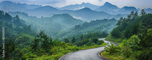 A picturesque scene of an asphalt road winding through lush green forests against the backdrop of majestic mountains. tranquil landscape captures the serene beauty of nature in the region,