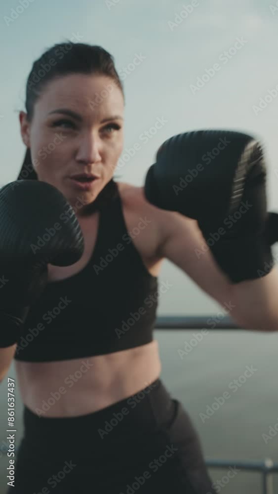Determined woman in her 30s, wearing activewear, training with boxing gloves outdoors to enhance her strength and fitness. Determined woman in her 30s, wearing activewear, training with boxing gloves outdoors to enhance her strength and fitness.