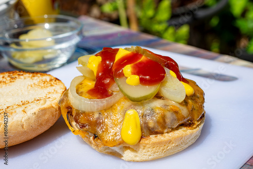 Straight from the grill, burger patty topped with cojack cheese, grilled onions, dill pickles, ketchup and mustard on a toasted bun. photo