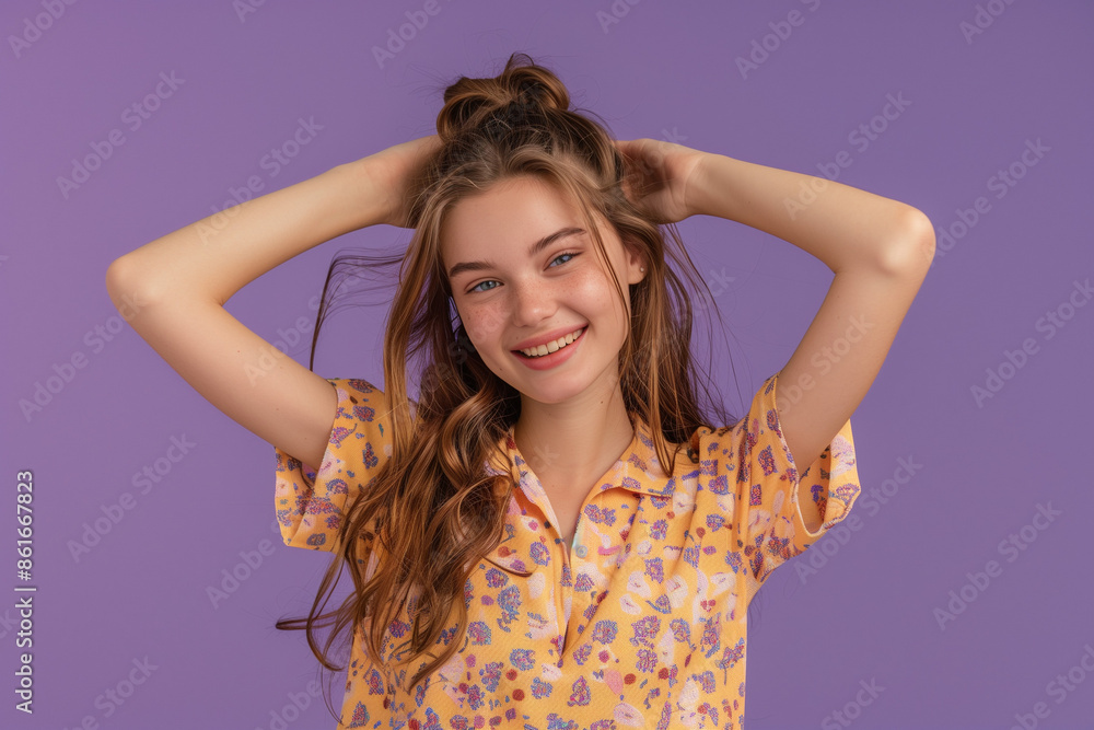 Fototapeta premium Portrait of a cheerful young girl in a floral shirt, touching her hair, set against a vibrant purple background, perfect for lifestyle and fashion content.
