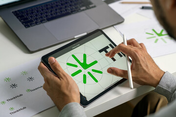 Close-up shot of a graphic designer making notes on logo designs, using a tablet, designing logos, and showcasing the corporate identity and logo design process.