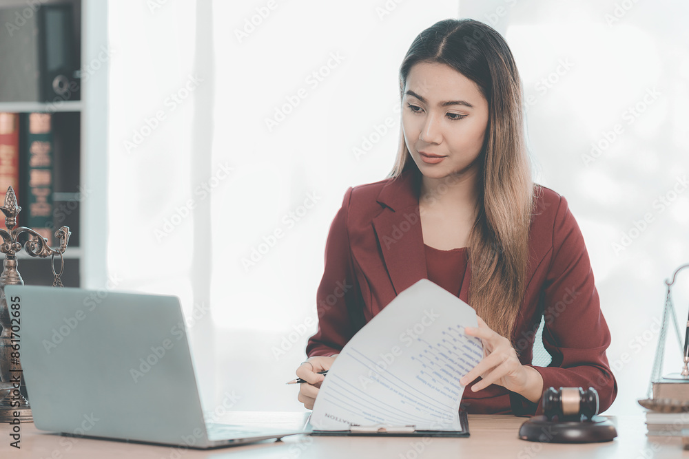 Female lawyer or judge checking documents or contracts and taking notes in notebook, working in law office with hammer and scale, laptop placed beside. Female lawyer or judge checking documents or contracts and taking notes in notebook, working in law office with hammer and scale, laptop placed beside.