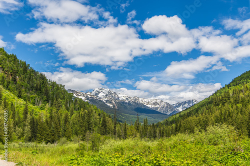 Landscape of the Purcell Mountains through Green Forests in British Columbia, Canada with Blue Sky and White Puffy Clouds in the Background