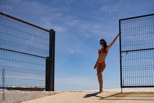 Stylish Brunette Woman in Black Sunglasses and Red Bikini Posing on a Rocky Seashore © sutulastock