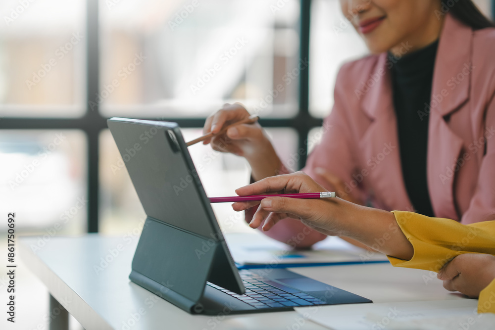 Two businesswomen collaborate in a modern office, using a digital tablet to discuss ideas and strategies Two businesswomen collaborate in a modern office, using a digital tablet to discuss ideas and strategies
