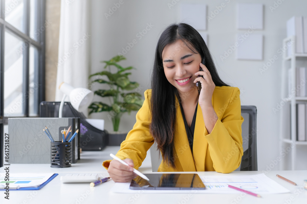 Asian businesswoman talking on phone and taking notes on tablet in office Asian businesswoman talking on phone and taking notes on tablet in office