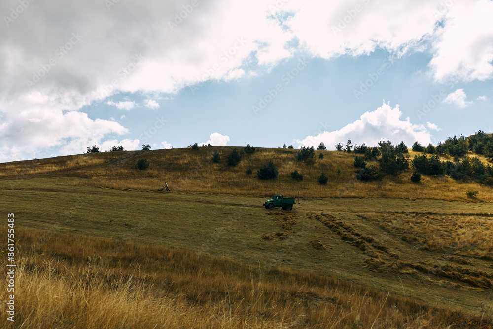 Obraz premium Picturesque countryside scene with a green truck parked on top of a grassy hill in the middle of a field