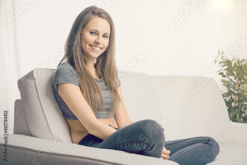 Free Download Beautiful young woman smiling while sitting on a sofa at home - GFXLoad