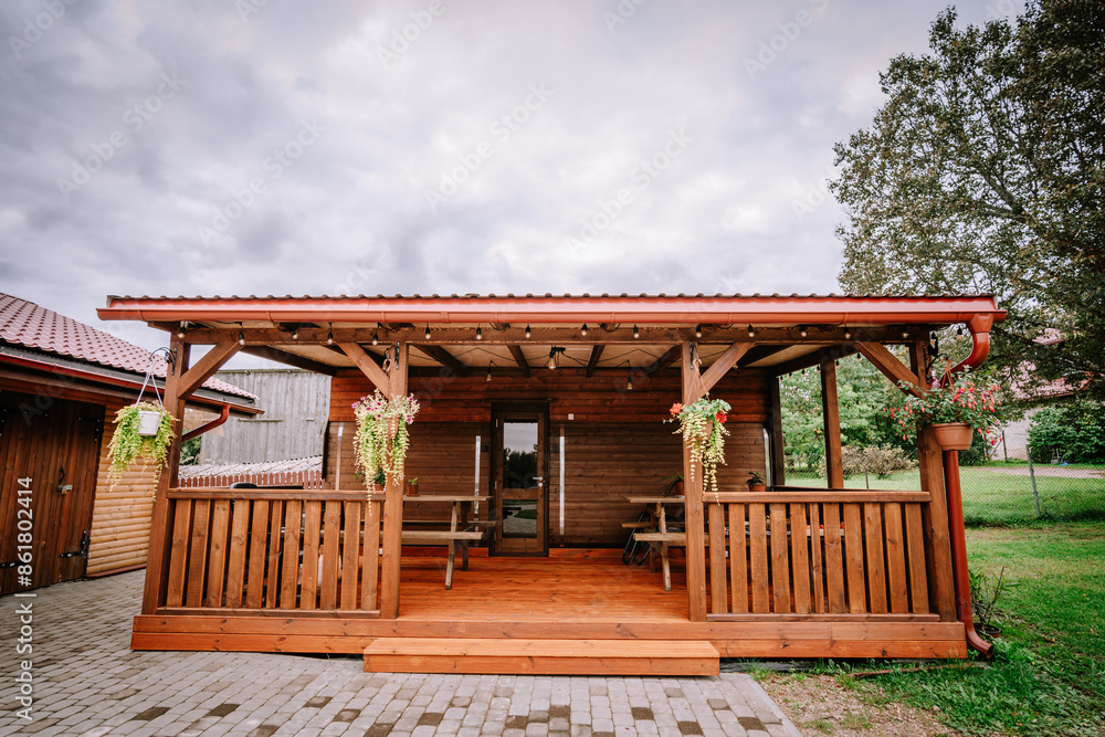 Wooden outdoor patio with hanging plants and picnic tables, set in a backyard under a cloudy sky. Copy space... Wooden outdoor patio with hanging plants and picnic tables, set in a backyard under a cloudy sky. Copy space...