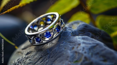 Silver ring with blue gemstones on a stone, against green backdrop, with detailed craftsmanship and elegant design