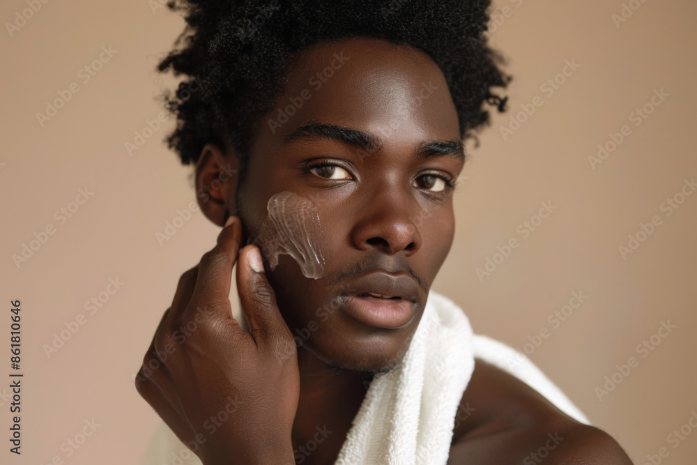 Obraz premium Young African American man applying facial lotion, towel over shoulder