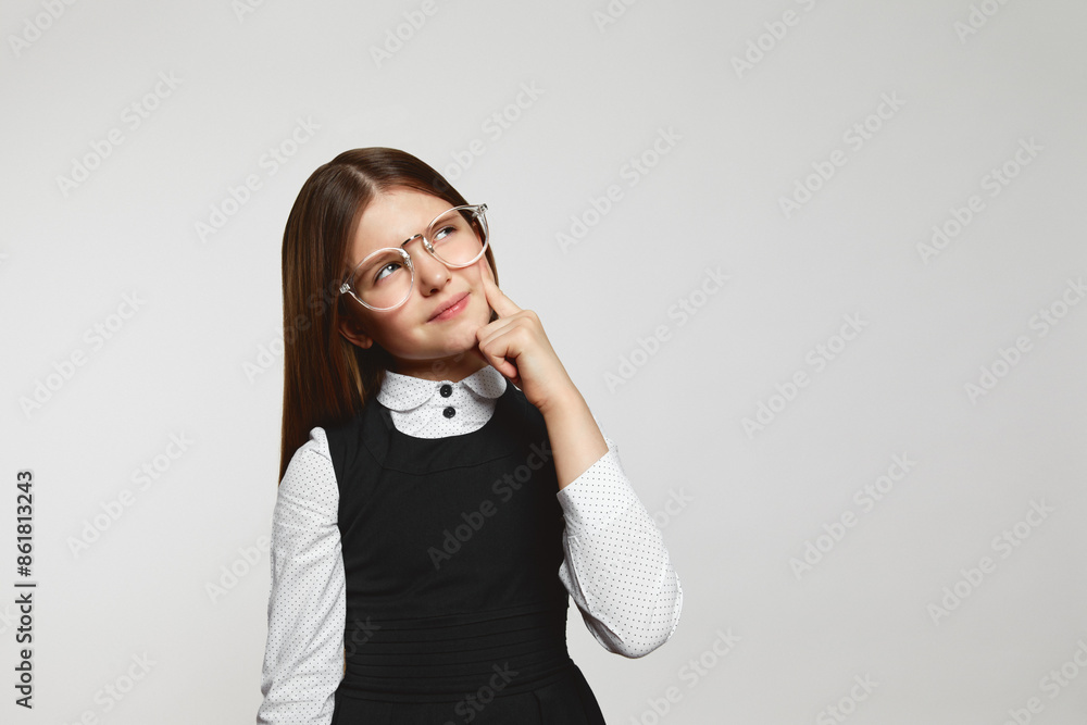 Doubtful schoolgirl with eyeglasses and uniform rubbing chin and looking away while thinking near empty space against white background Doubtful schoolgirl with eyeglasses and uniform rubbing chin and looking away while thinking near empty space against white background