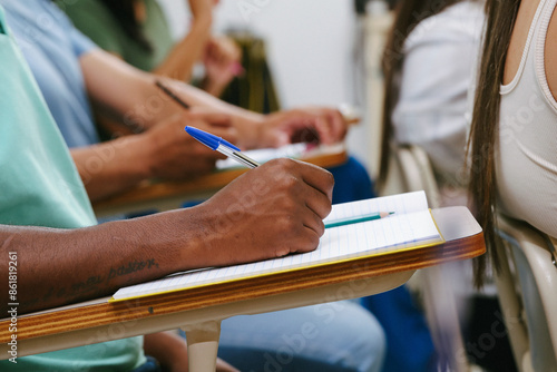 Closeup of male student hands on the school table in the classroom writing to notebook.