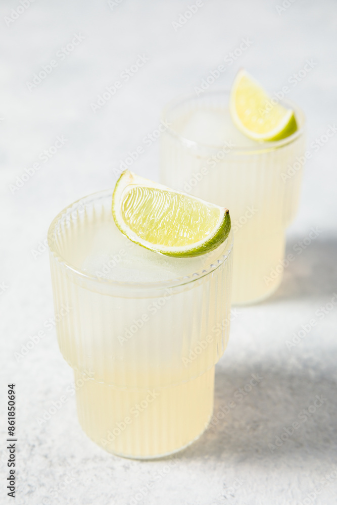 Refreshing lime cocktails on white table. Glass of citrus hard seltzer with ice cube and fresh lime slices. Summer lemonade, mocktail, vitamin water concept. Daiquiri, gimlet, caipirinha Refreshing lime cocktails on white table. Glass of citrus hard seltzer with ice cube and fresh lime slices. Summer lemonade, mocktail, vitamin water concept. Daiquiri, gimlet, caipirinha