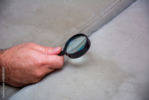 An unrecognizable hand examines a strand of hair on the couch with a magnifying glass