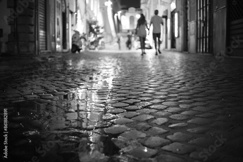 Couple walks away hand in hand aom wet cobbled street in Rome