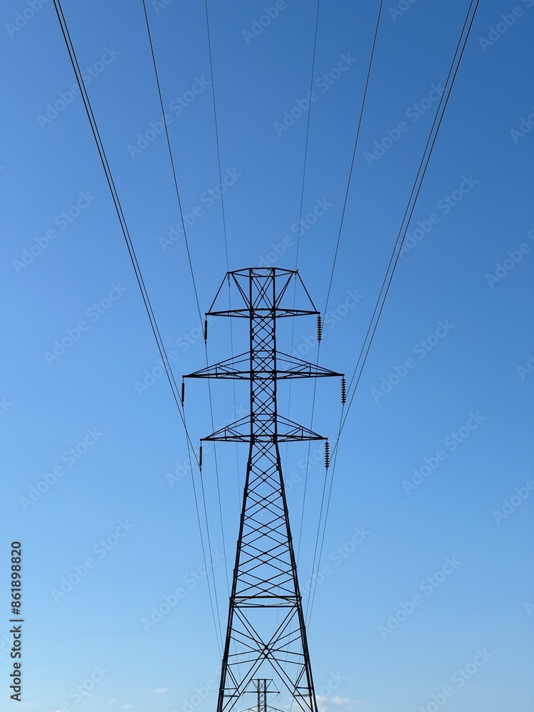 A tall power tower is silhouetted against a blue sky A tall power tower is silhouetted against a blue sky