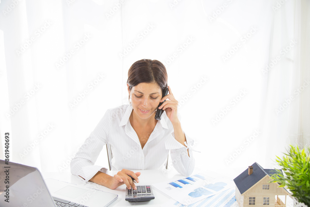 Good business talk. Cheerful young beautiful woman in glasses talking on mobile phone and using laptop with smile while sitting at her working place Good business talk. Cheerful young beautiful woman in glasses talking on mobile phone and using laptop with smile while sitting at her working place