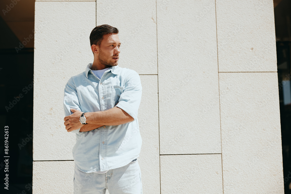 Confident young man in casual attire standing against a modern white wall, looking to the side with a thoughtful expression Confident young man in casual attire standing against a modern white wall, looking to the side with a thoughtful expression