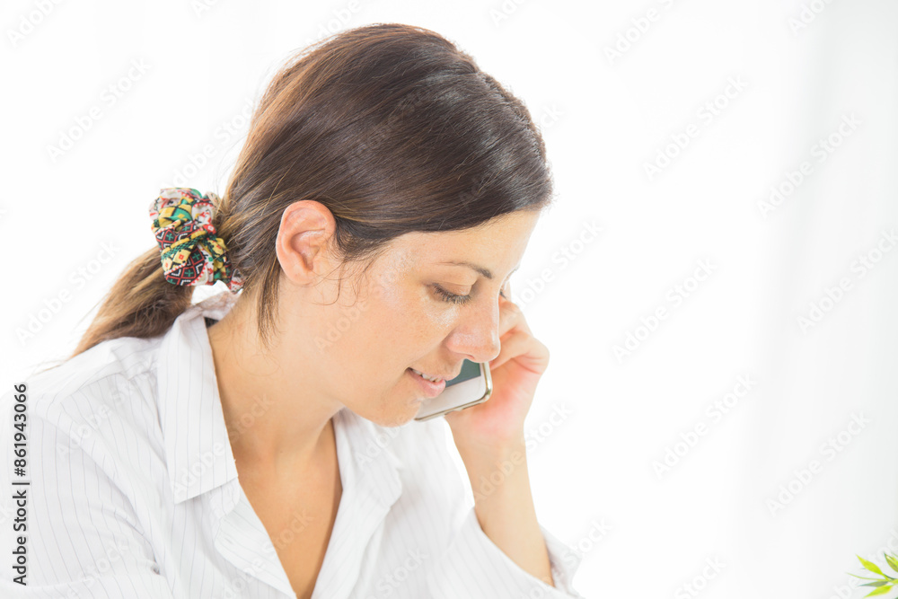 Good business talk. Cheerful young beautiful woman in glasses talking on mobile phone and using laptop with smile while sitting at her working place