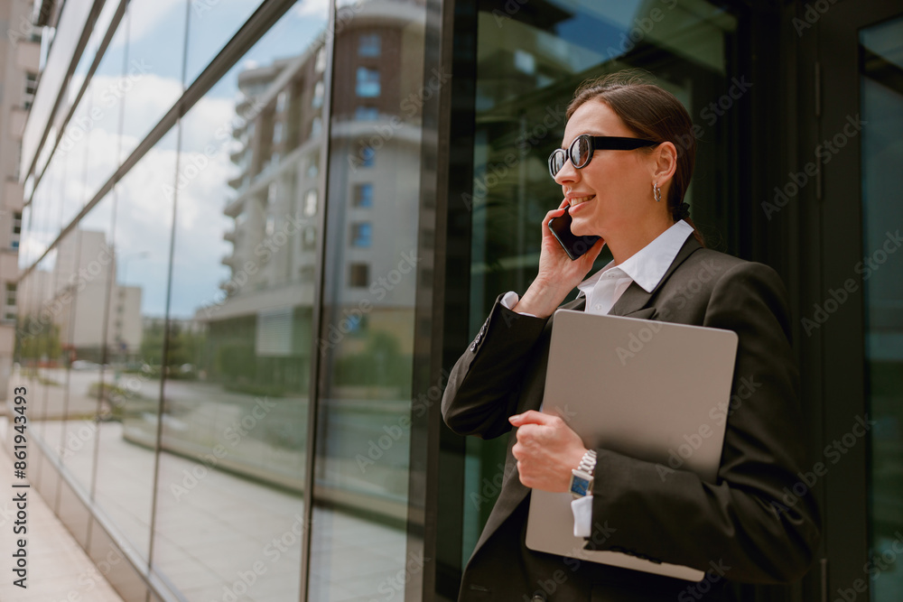 A confident businesswoman is multitasking, talking on the phone and holding a laptop A confident businesswoman is multitasking, talking on the phone and holding a laptop