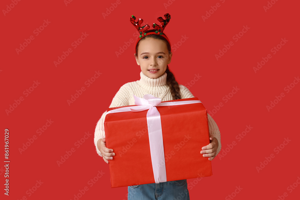 Cute little girl in reindeer horns with Christmas gift on red background Cute little girl in reindeer horns with Christmas gift on red background