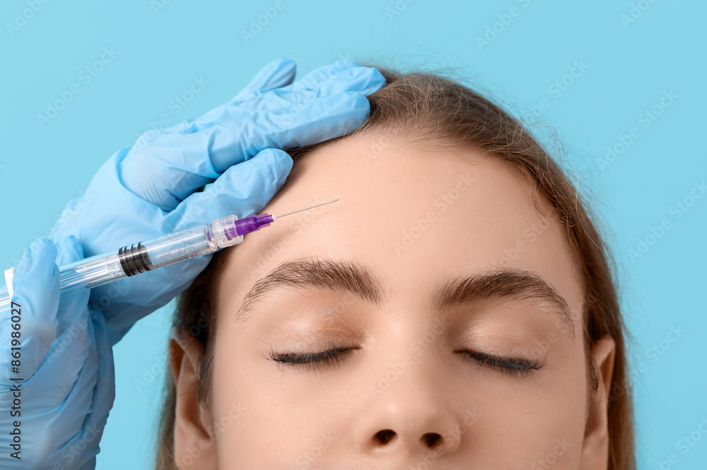 Young woman receiving filler injection in forehead on blue background Young woman receiving filler injection in forehead on blue background