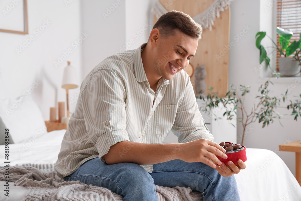 Handsome man with heart-shaped chocolate candies in bedroom Handsome man with heart-shaped chocolate candies in bedroom