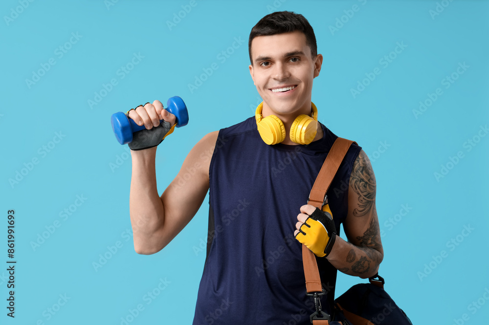 Young man with sports bag and dumbbell on blue background Young man with sports bag and dumbbell on blue background