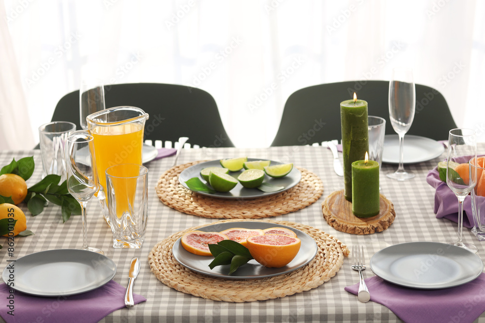 Beautiful table setting with citrus fruits, candles and juice on checkered tablecloth in living room Beautiful table setting with citrus fruits, candles and juice on checkered tablecloth in living room