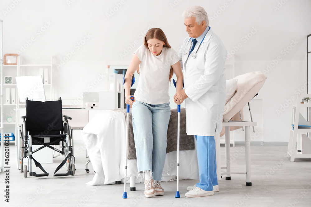 Mature doctor helping female patient with crutches in clinic Mature doctor helping female patient with crutches in clinic