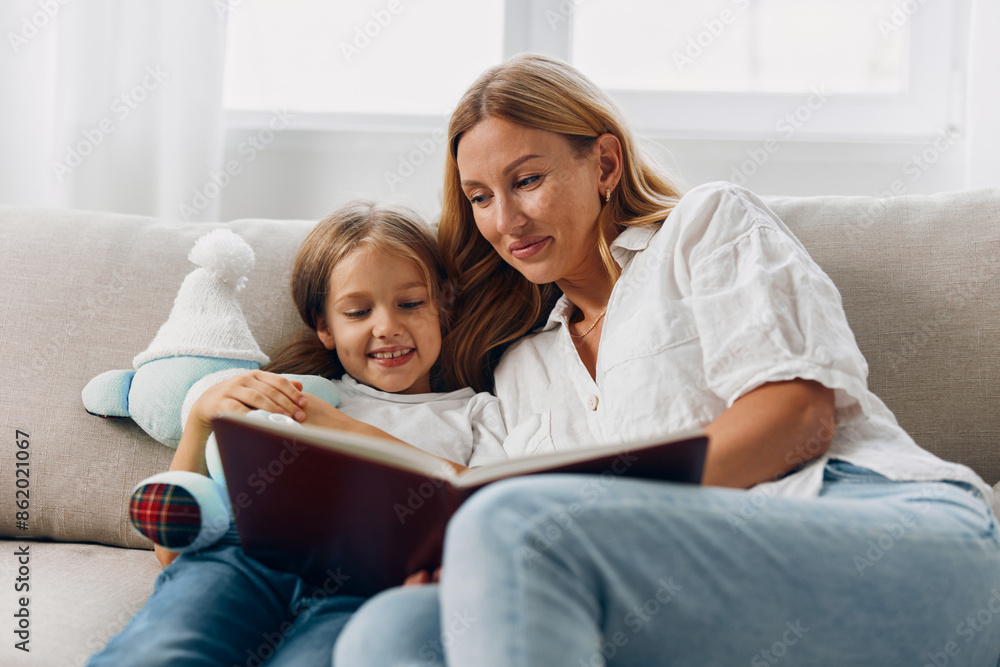 Mother and daughter sharing a cozy moment on the couch while reading a book together Mother and daughter sharing a cozy moment on the couch while reading a book together