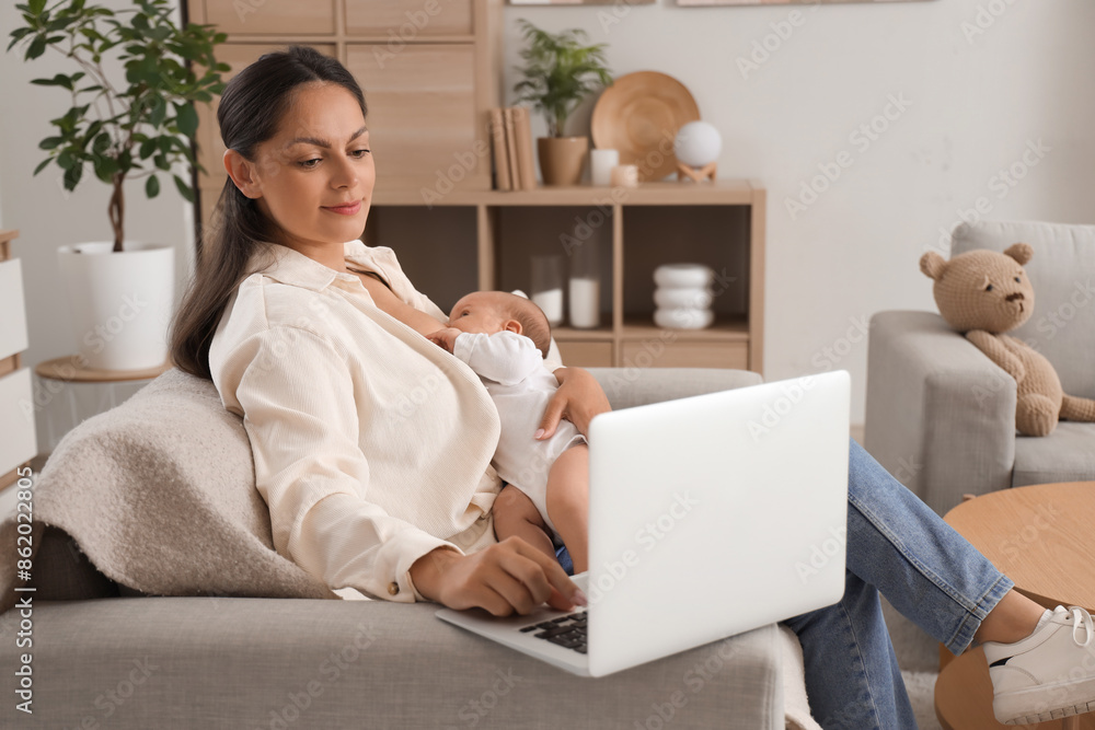 Naklejka premium Mother breastfeeding her baby while using laptop on sofa at home