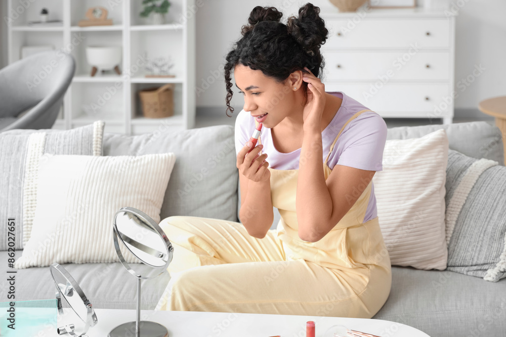 Beautiful young African-American woman with lipstick doing makeup at home