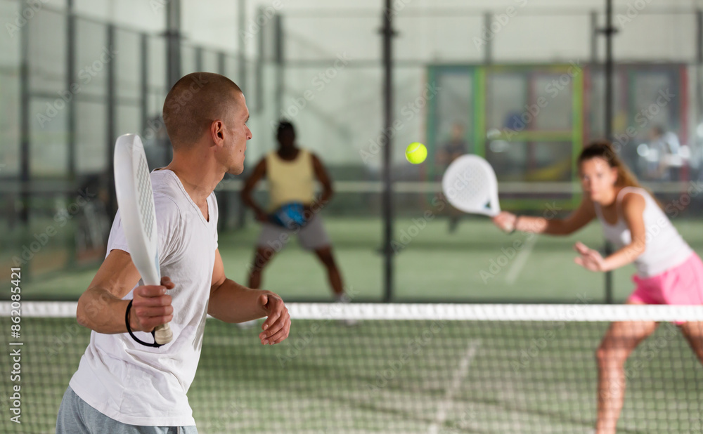 Φωτογραφία Rear view of man playing doubles paddle tennis match on indoor court on blurred background of opponents