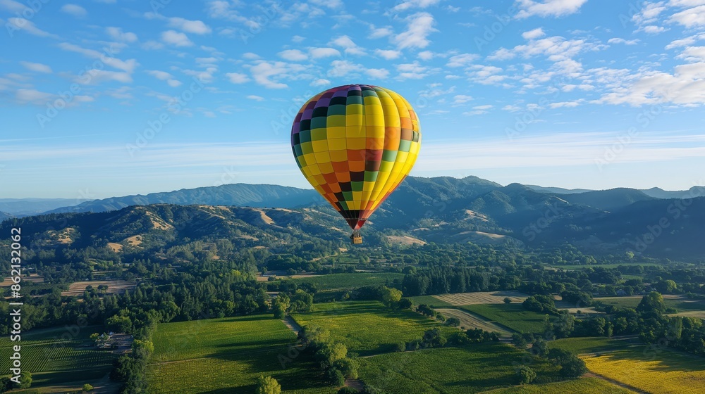 Fototapeta premium Hot air balloon over green fields under blue sky.