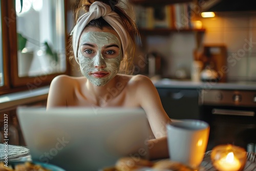 A woman with a towel on her head and a facial mask works dedicatedly on her laptop at home, depicting multitasking and a blend of work and relaxation in a cozy setting. photo