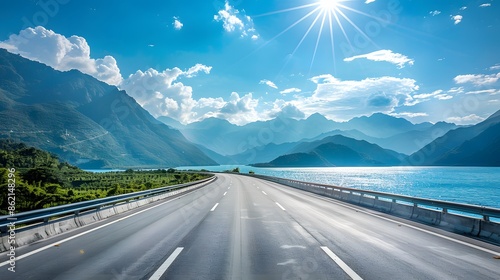 A beautiful highway with mountains and sea in the background, on a sunny day with a blue sky. The asphalt road had clear white lines on the edges of the photo with a sea view from behind.