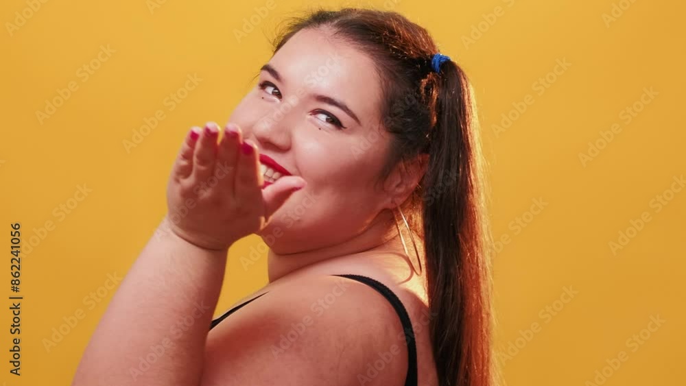 Body positivity. Optimistic people. Confidence woman. Curvy overweight charming flirting girl turning around blowing kiss smiling winking isolated on yellow background. Body positivity. Optimistic people. Confidence woman. Curvy overweight charming flirting girl turning around blowing kiss smiling winking isolated on yellow background.