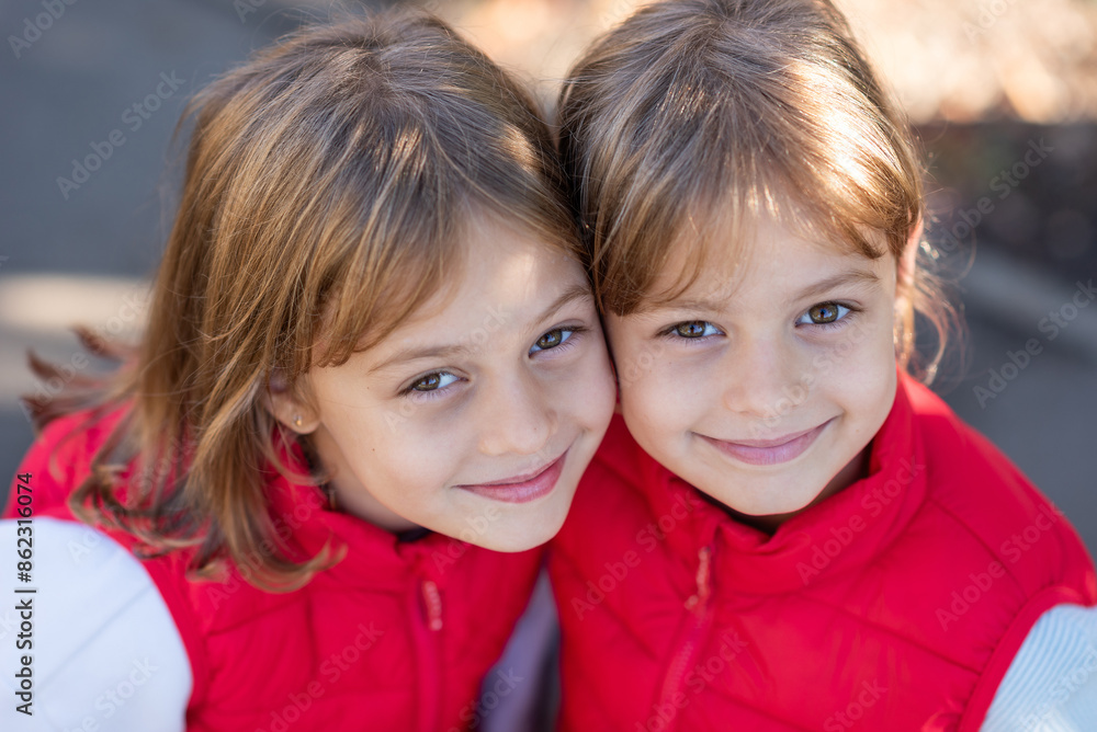 Portraits of two twin girls in red vests and with yellow autumn leaves in their hands. Kindergarten Portraits of two twin girls in red vests and with yellow autumn leaves in their hands. Kindergarten